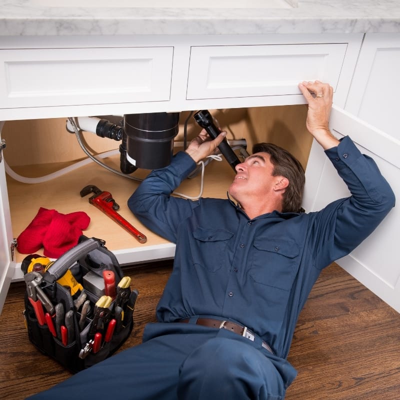 Male plumber checking under a sink for a leak
